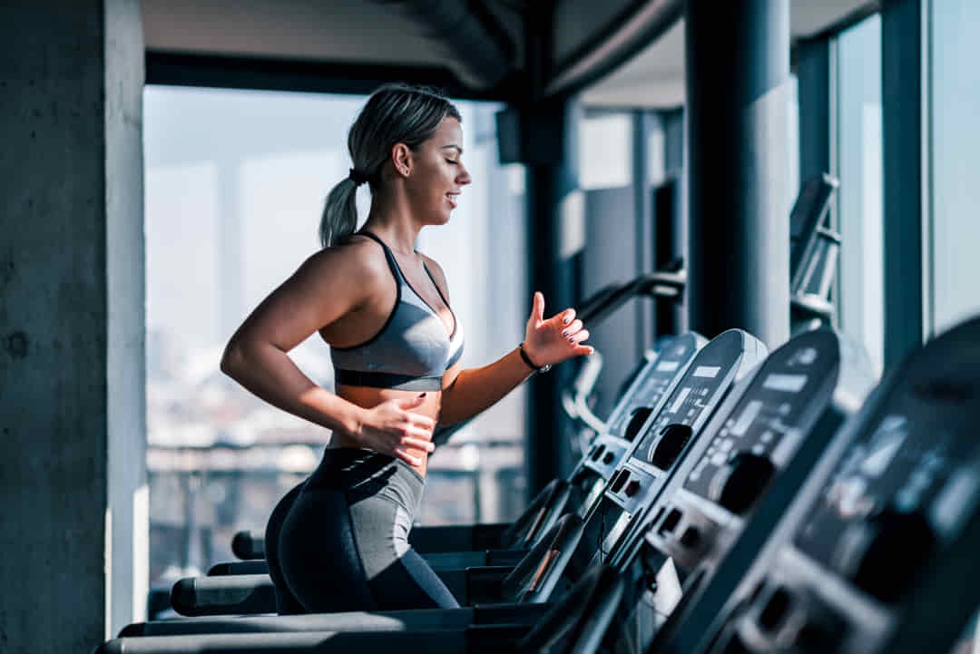 Mujer corre a ritmo constante en la cinta junto a los ventanales de nuestro gimnasio en Barcelona, centrada en trabajo cardiovascular y quema de grasa