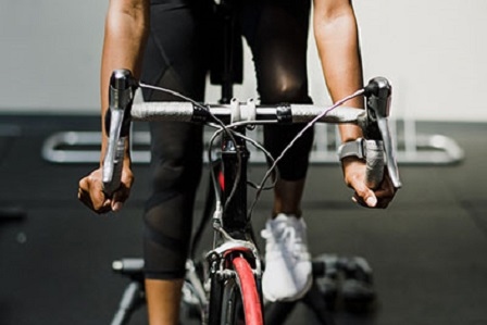 Primer plano de las manos de un deportista sobre el manillar durante una sesión de bicicleta indoor en nuestro gimnasio de Barcelona, enfocada en trabajo cardiovascular de alta intensidad