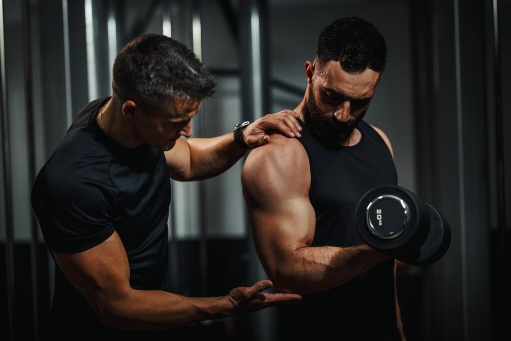 Entrenador corrige la posición del brazo mientras un cliente ejecuta un curl de bíceps con mancuerna de 20 kg en nuestro estudio de Barcelona