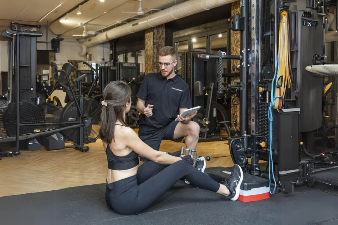 Entrenador personal guiando a una clienta en ejercicio de remo con polea en nuestro gimnasio de Barcelona