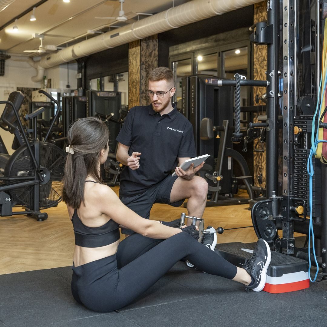 Entrenador personal guiando a una clienta en ejercicio de remo con polea en nuestro gimnasio de Barcelona