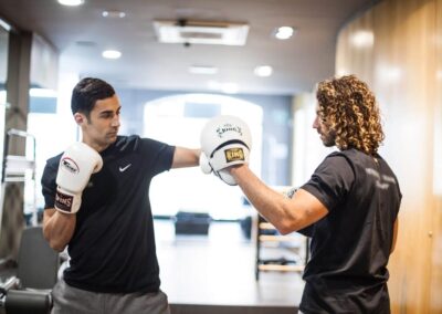 Sesión privada de boxeo: el entrenador sostiene las manoplas mientras el alumno conecta un directo en nuestro estudio de Barcelona
