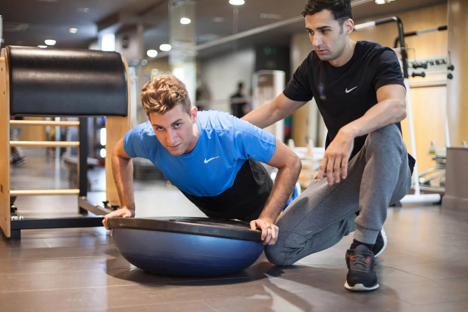 Entrenador personal ajusta la técnica de un cliente que realiza flexiones sobre un bosu para trabajar core y equilibrio en nuestro gimnasio de Barcelona