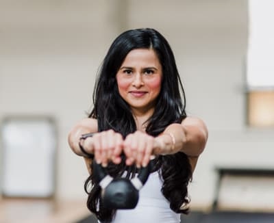 Mujer realiza una elevación frontal con kettlebell, activando hombros y core, durante su sesión en nuestro gimnasio de Barcelona